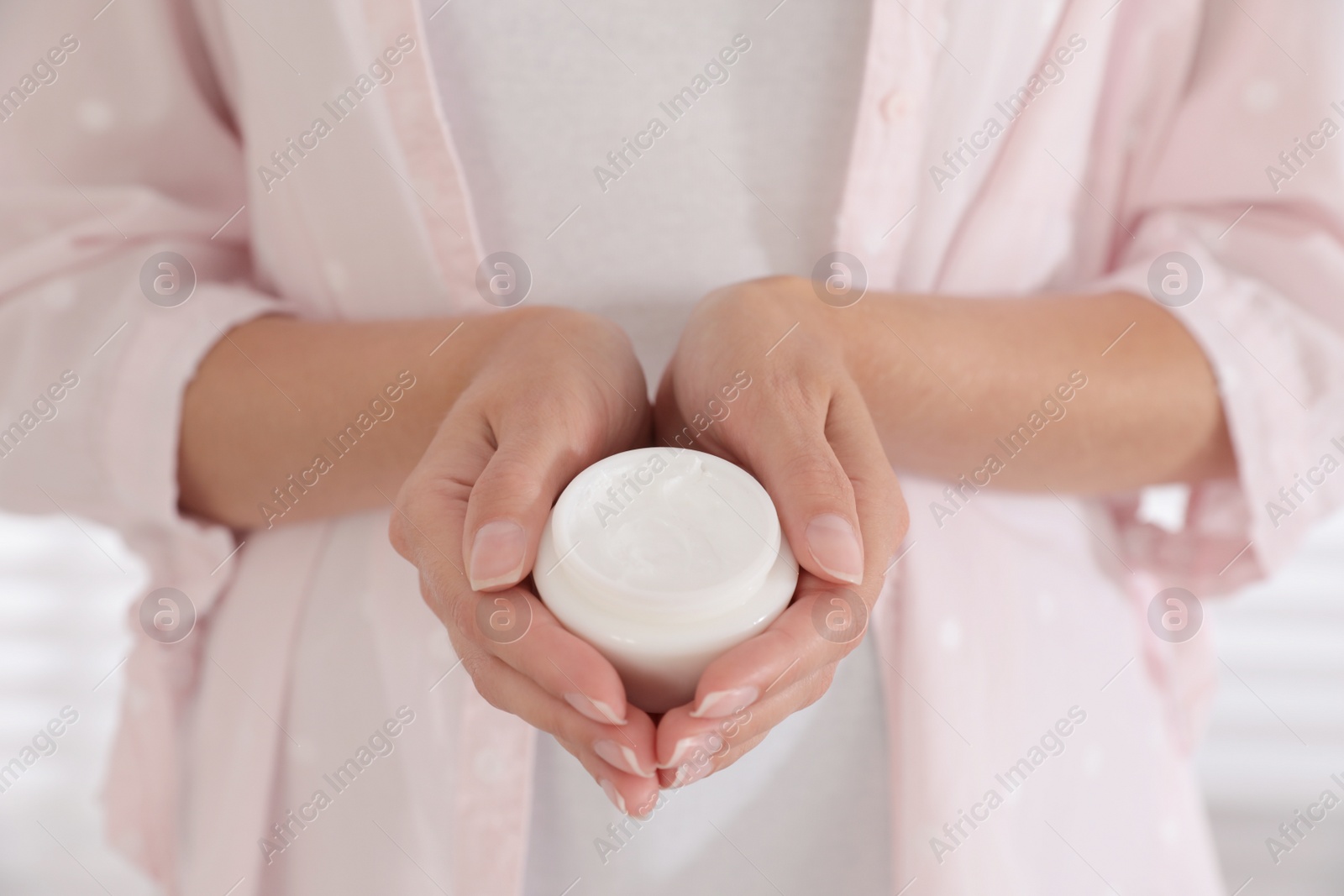 Photo of Woman holding jar with cream near window, closeup