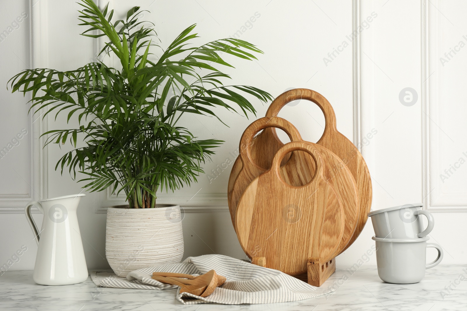 Photo of Wooden cutting boards, spoons, dishware and houseplant on white marble table