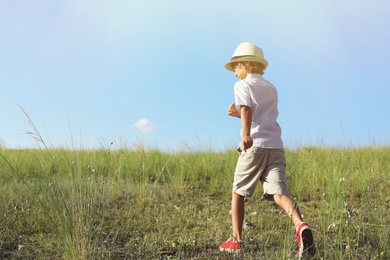Photo of Cute little boy wearing stylish hat outdoors, space for text. Child spending time in nature
