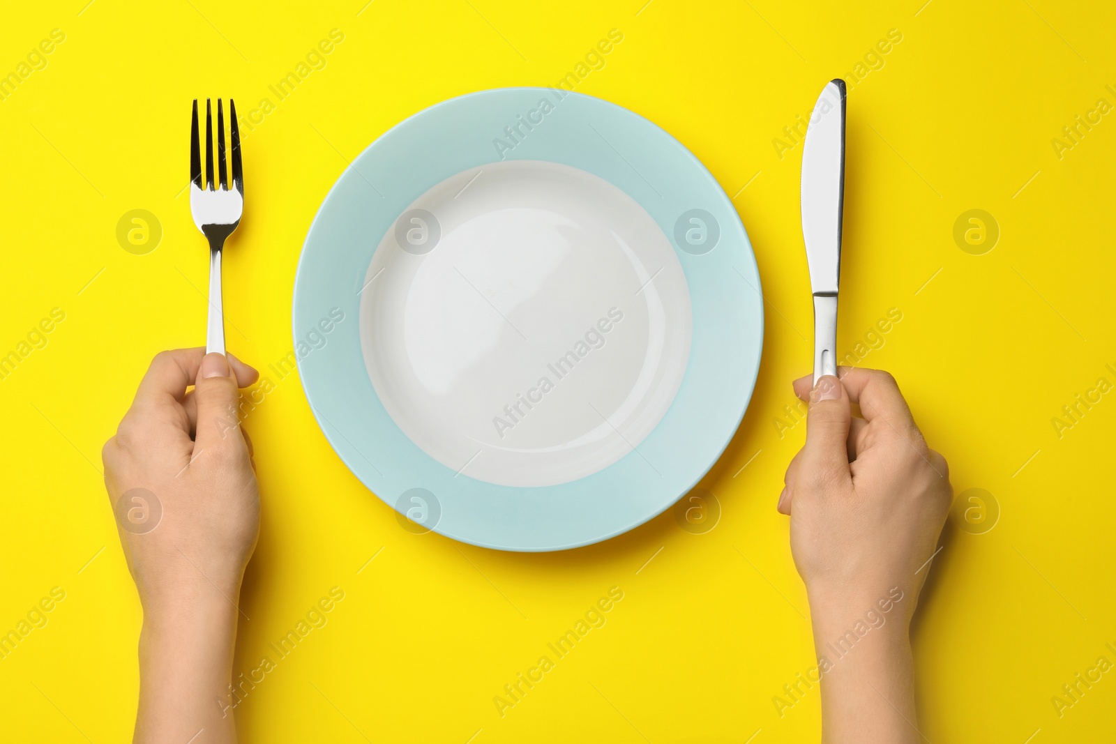 Photo of Woman with fork, knife and empty plate on color background, top view