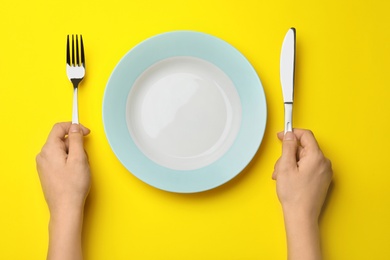 Woman with fork, knife and empty plate on color background, top view