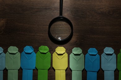 Photo of Many colorful paper figures and magnifying glass on wooden table, flat lay. Recruiter searching employee