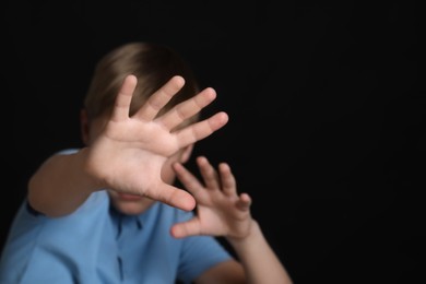 Boy making stop gesture against black background, focus on hands and space for text. Children's bullying