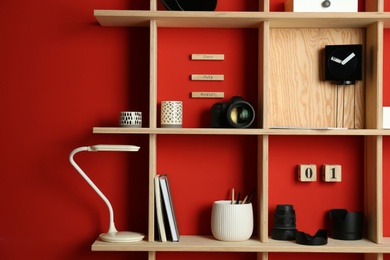 Photo of Stylish wooden shelves with photography equipment and decorative elements on red wall