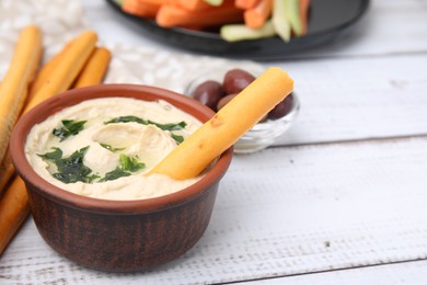 Photo of Delicious hummus with grissini sticks on white wooden table. Space for text