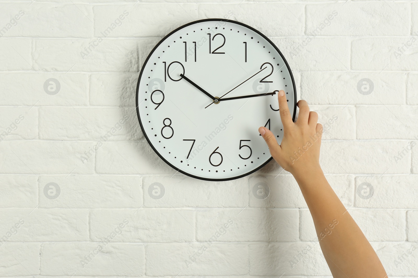 Photo of Woman touching clock on white brick wall. Time management