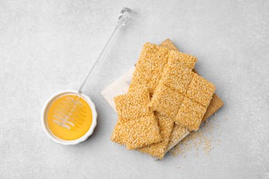 Delicious sesame kozinaki bars and honey on light grey table, flat lay