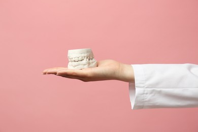 Doctor holding dental model with jaws on pink background, closeup. Cast of teeth