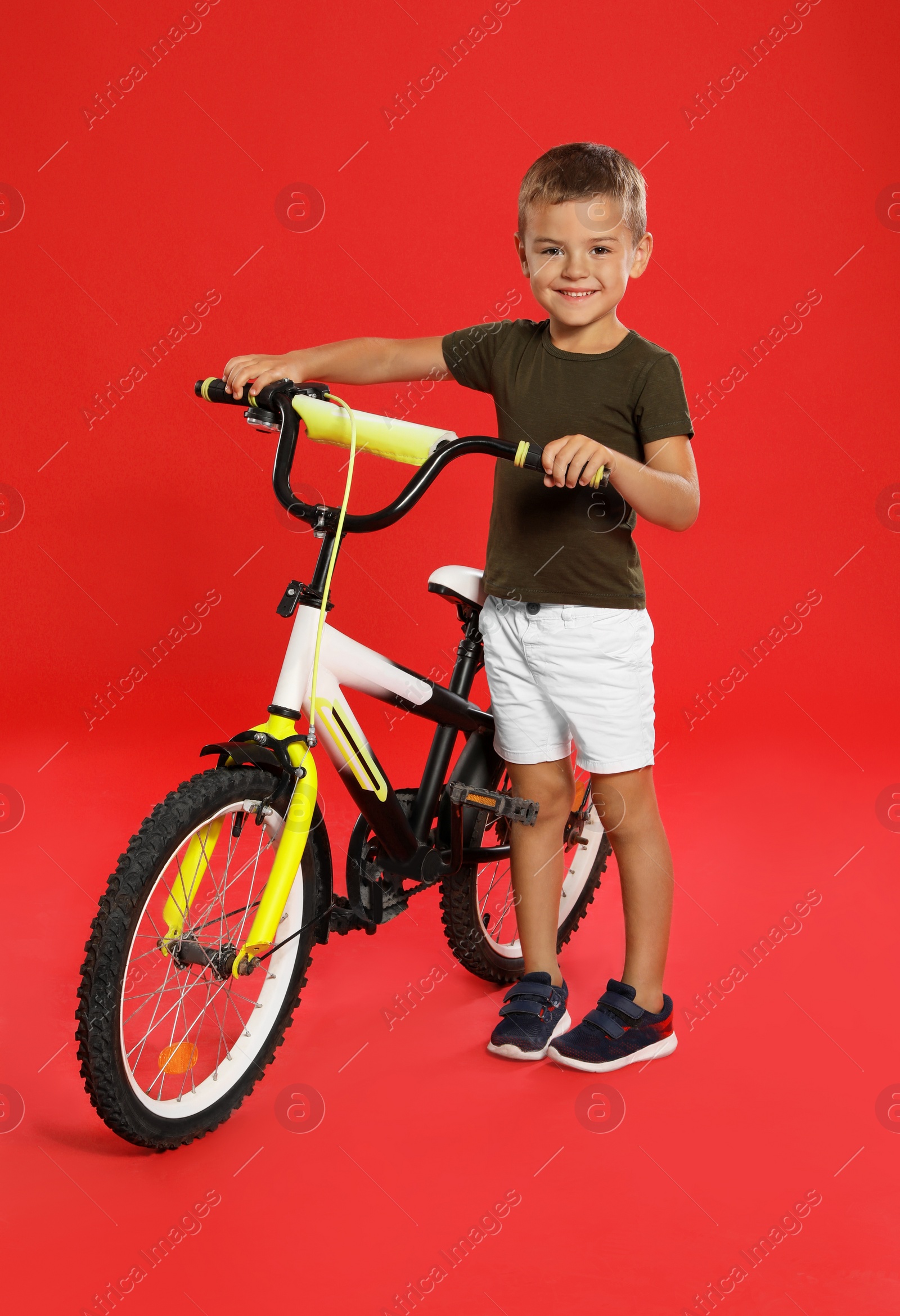 Photo of Cute little boy with bicycle on red background