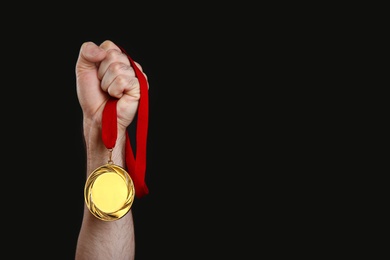 Man holding golden medal on black background, closeup. Space for design