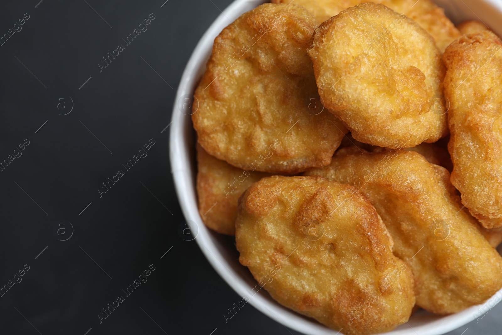 Photo of Bucket with tasty chicken nuggets on black table, top view