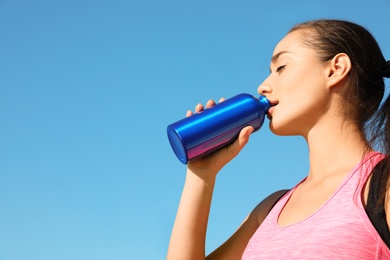 Young sporty woman drinking from water bottle outdoors on sunny day. Space for text