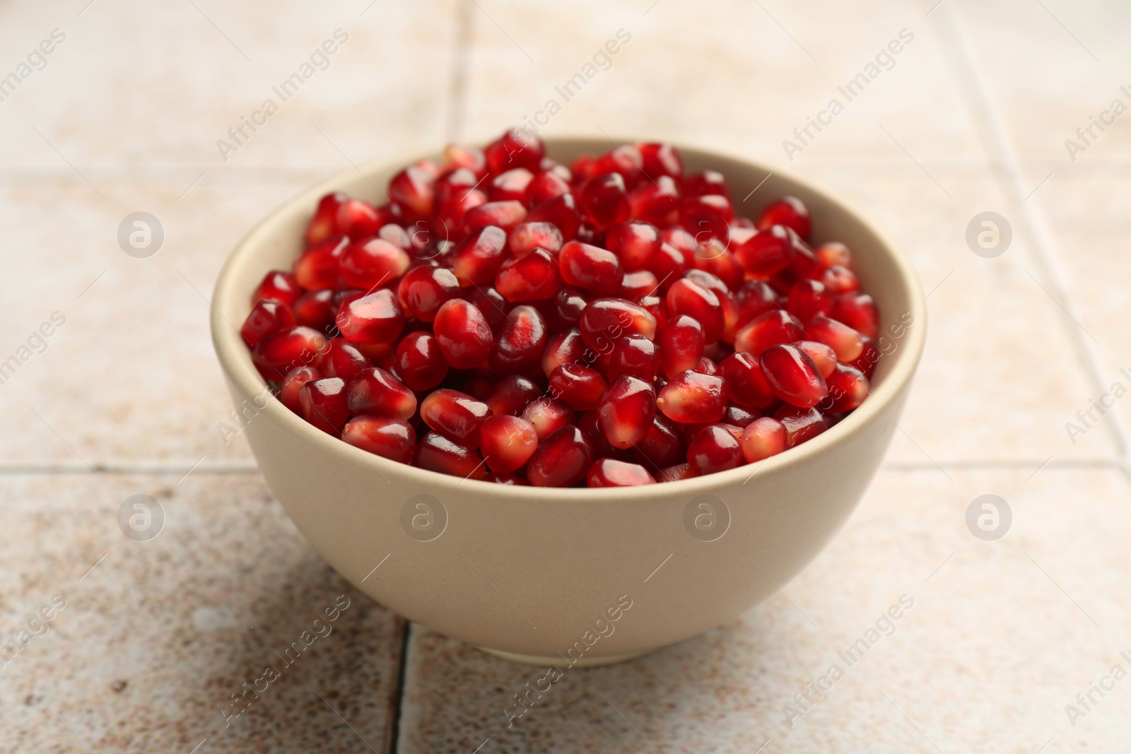 Photo of Tasty ripe pomegranate grains on tiled table, closeup