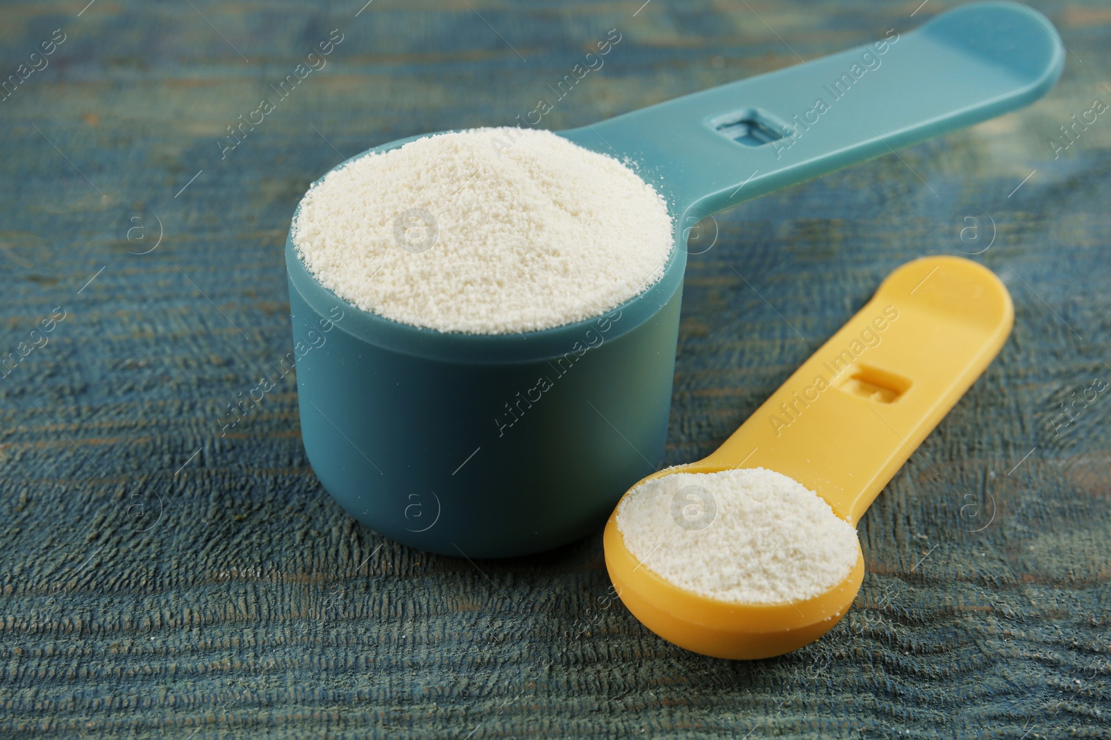 Photo of Measuring scoops of protein powder on blue wooden table, closeup