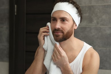 Washing face. Man with headband and towel in bathroom