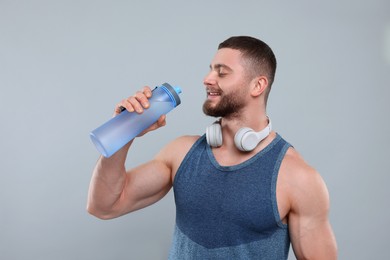 Photo of Handsome sportsman with headphones and bottle of water on grey background, space for text
