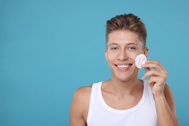 Handsome man with cotton pad on light blue background, space for text