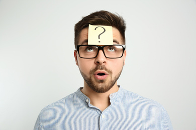 Emotional man with question mark sticker on forehead against light background