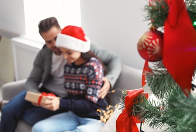 Photo of Christmas tree and happy young couple with gift box on sofa at home