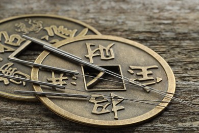 Photo of Acupuncture needles and ancient coins on wooden table, closeup