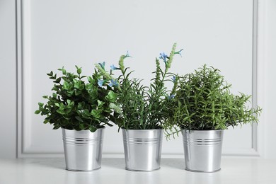 Photo of Different artificial potted herbs on wooden table near white wall