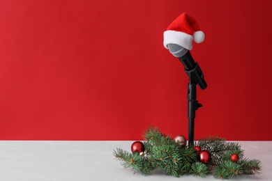 Photo of Microphone with Santa hat and festive decor on table against red background, space for text. Christmas music
