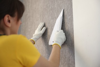 Photo of Woman smoothing stylish gray wallpaper in room, closeup