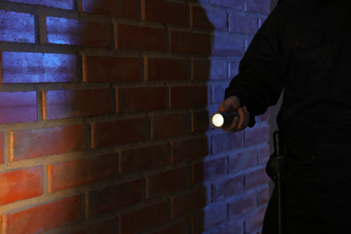 Photo of Male security guard with flashlight near brick wall in darkness