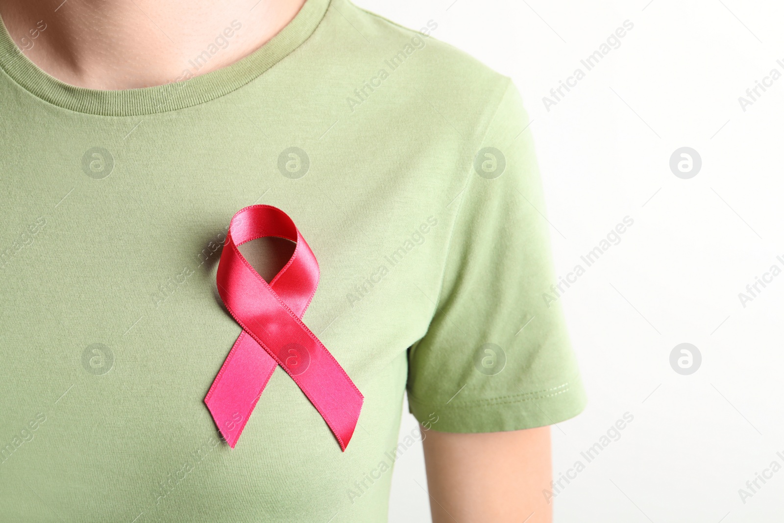 Photo of Woman with pink ribbon on t-shirt against light background. Cancer awareness