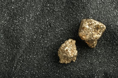 Photo of Shiny gold nuggets on black sand, top view. Space for text