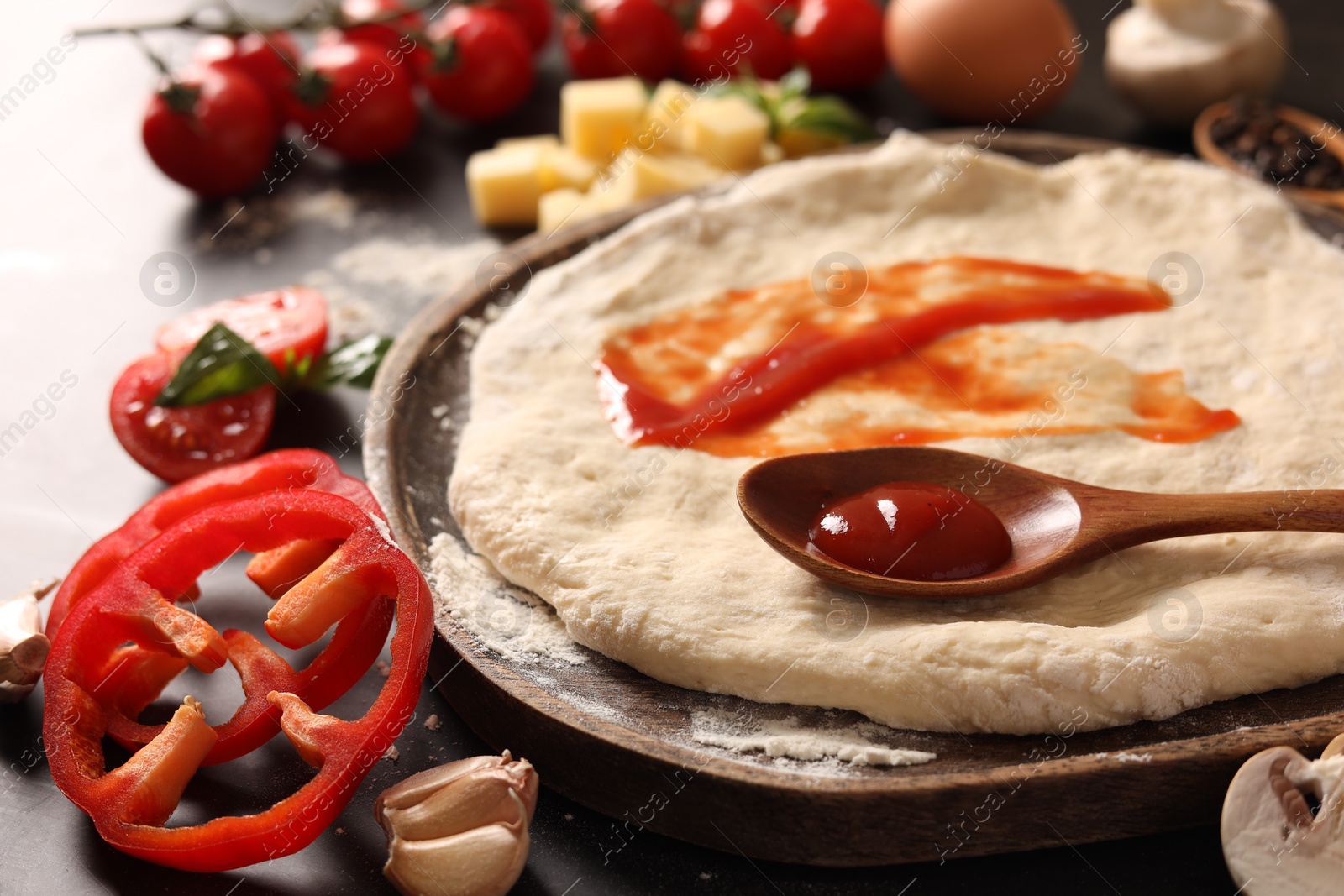 Photo of Pizza dough with tomato sauce and products on dark table, closeup