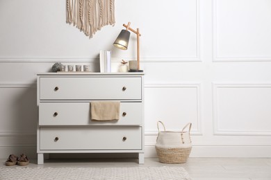 Stylish room interior with chest of drawers near white wall