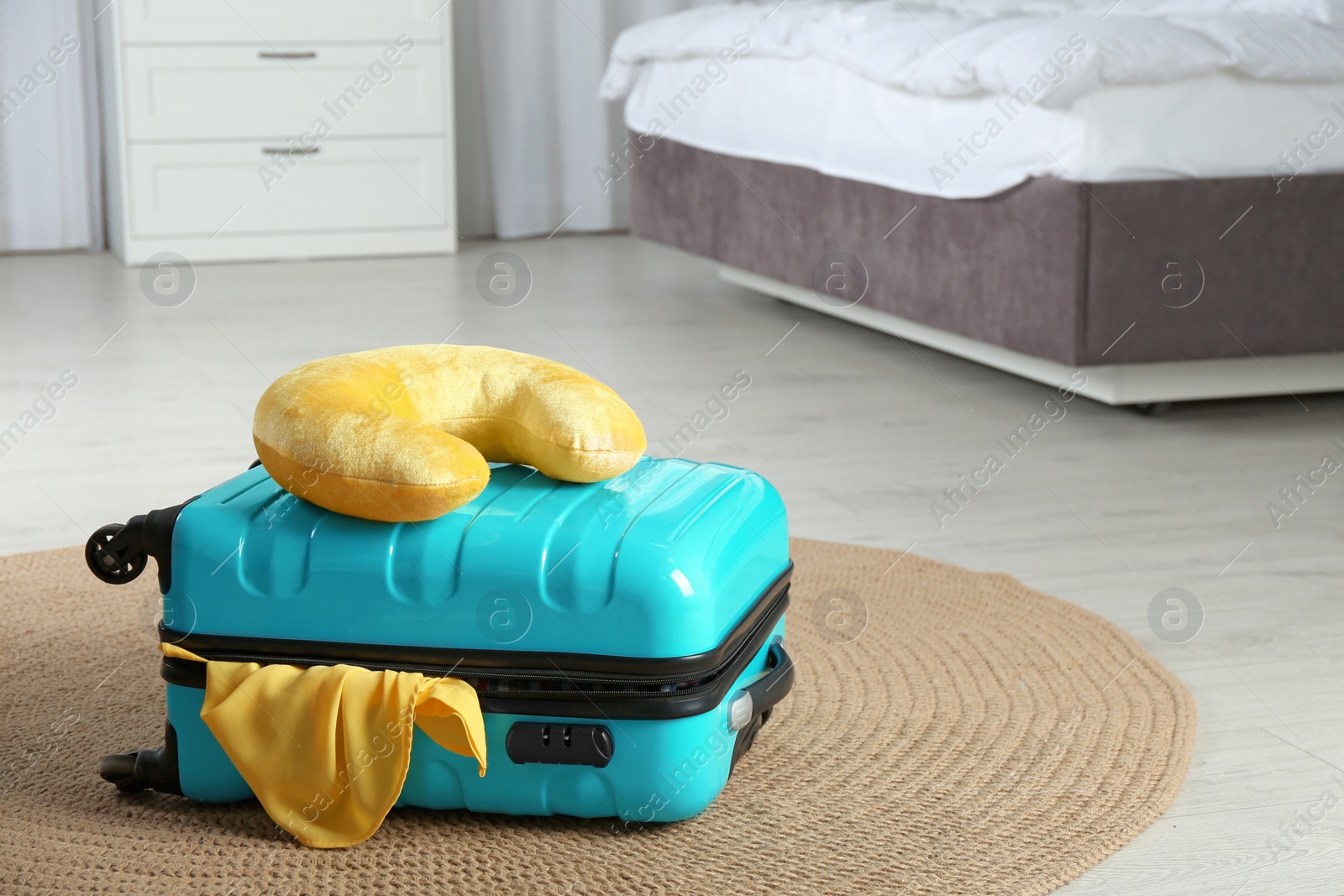 Photo of Suitcase with clothes and travel pillow in bedroom