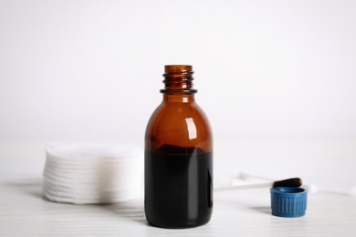 Photo of Bottle of medical iodine, cotton pads and buds on white wooden table