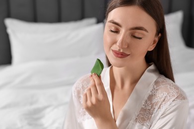 Photo of Young woman applying aloe gel from leaf onto her skin indoors. Space for text