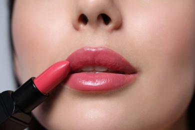 Photo of Closeup view of young woman applying beautiful glossy lipstick