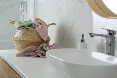 Photo of Wicker laundry basket with towels near sink on countertop in bathroom