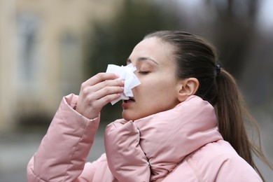 Photo of Ill woman with paper tissue sneezing outdoors