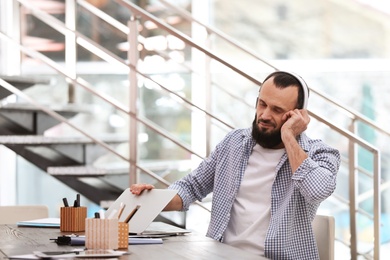 Photo of Mature man with headphones and laptop working in home office