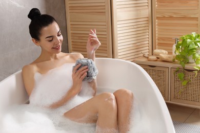 Photo of Woman taking bath with mesh pouf indoors
