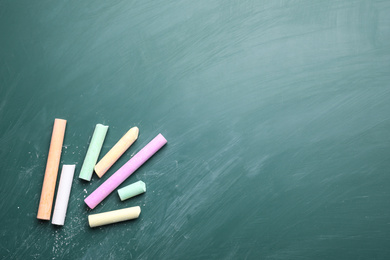 Photo of Pieces of color chalk on greenboard, flat lay. Space for text