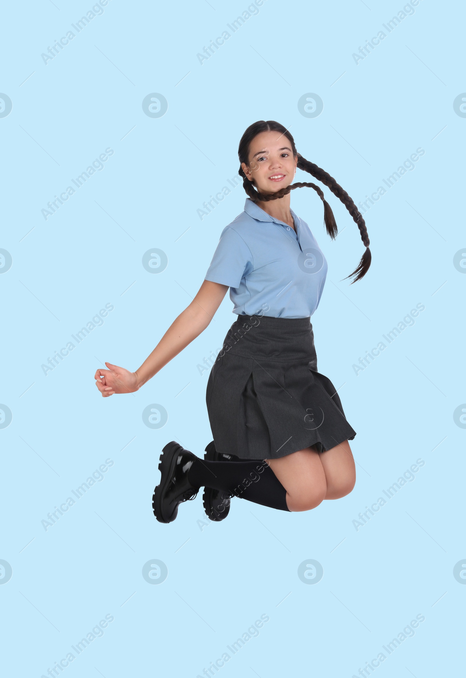 Image of Happy cute girl in school uniform jumping on light blue background