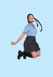 Happy cute girl in school uniform jumping on light blue background