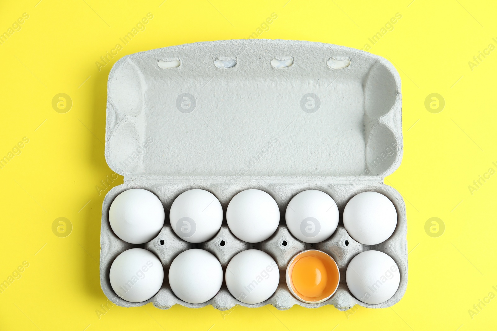 Photo of Fresh chicken eggs in box on yellow background, top view