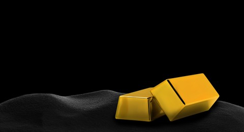 Image of Shiny gold bars on black sand, space for text