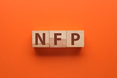 Photo of Abbreviation NFP (Nonfarm Payroll) made with wooden cubes on orange background, flat lay