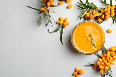 Photo of Delicious sea buckthorn jam and fresh berries on light grey table, flat lay. Space for text