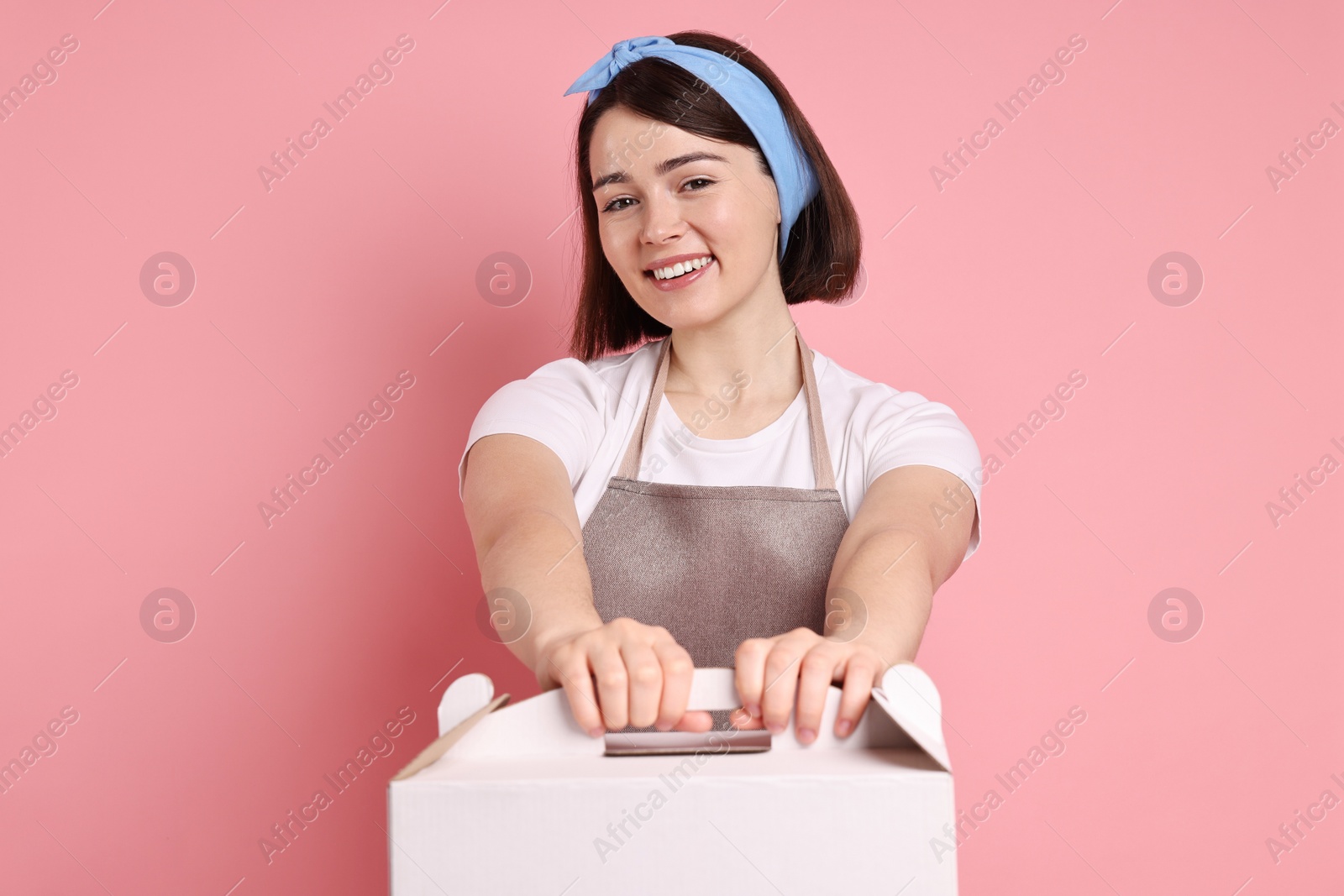 Photo of Happy confectioner with cake box on pink background