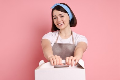 Photo of Happy confectioner with cake box on pink background