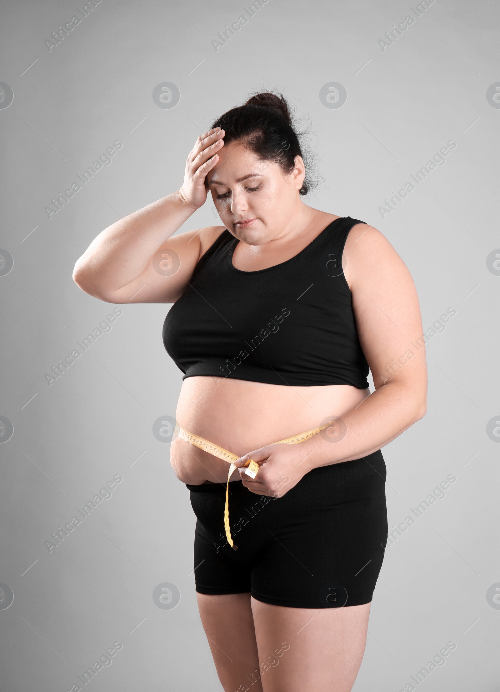 Photo of Fat woman with measuring tape on grey background. Weight loss